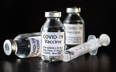 Coronavirus Covid-19 vaccine concept -  three glass vials on black table, hypodermic syringe needle near, closeup detail (label own design - dummy data, not real product)