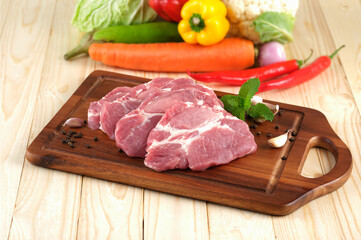 Pork neck Slice on wooden plate on wooden table with vegetables on background