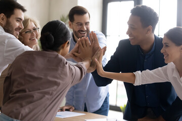 Happy diverse employees team joining hands, celebrating teamwork success, business achievement at meeting, showing unity and support, engaged in team building activity at corporate briefing