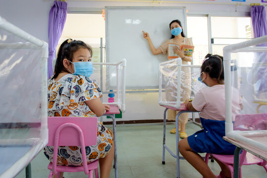 Asian school children wear medical masks, social distancing in classrooms and schools that are about to begin. There are plastic sheets between students studying together.