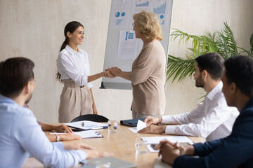 Fototapeta premium Mature executive shaking Arabic businesswoman hand at corporate meeting, middle aged team leader congratulating successful employee with job promotion, thanking for good result, hiring new worker