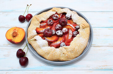 Homemade summer cake, galette with cherries and peaches on a gray plate on a wooden background.