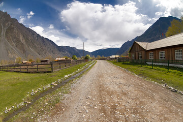 village road in a rural area in the mountains. high mountains, white clouds in a blue sky, summer landscape