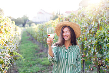 Woman with wineglass of pink wine in vineyard at sunset. Wine tasting in winery. Traveler enjoying...