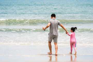 Asian father and daughter hold hand together walk on beach to sea