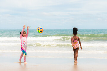 Asian and African American children play ball together on beach