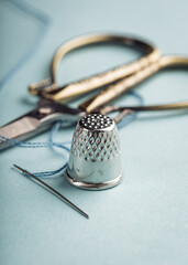 Vintage silver metal thimble and needle, scissors on blue background
