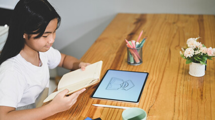 A schoolgirl is doing an E-Learning with a computer tablet at the wooden working desk.