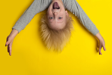 Screaming boy with blond long hair hanging upside down. Yellow background