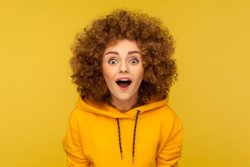 Oh my god, wow! Portrait of surprised curly-haired woman in urban style hoodie looking at camera...