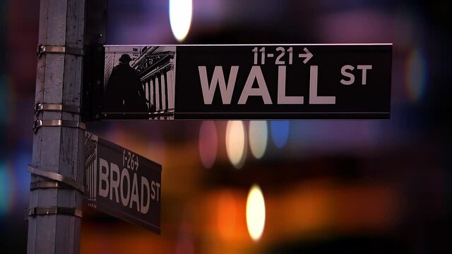City lights defocused behind the wall street signpost in lower Manhattan, New York City, USA.
