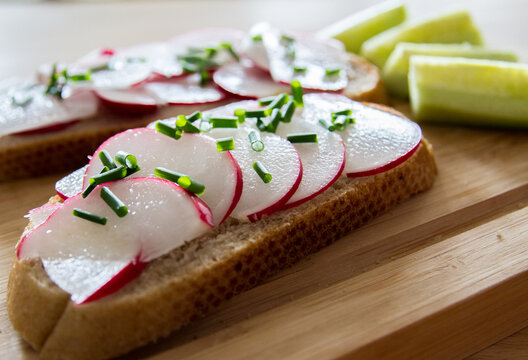 Healthy vegan or vegetarian snack: Bread with butter, radish and chives on wooden plate