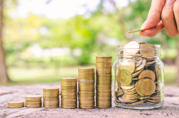 investor business man hand putting money on coins row stack on wood table with blur nature park background. money saving concept for financial banking and accounting.