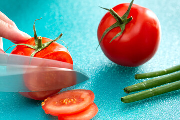 Cook slices the tomato with a knife on a cutting board.