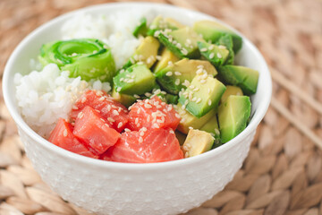 Hawaiian poke bowl with smoked salmon lox, avocado, white rice, cucumber and sesame seeds. Bright and airy feel 