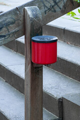 ein am h&ouml;lzernen Treppengel&auml;nder befestigter roter Ascher im Au&szlig;enbereich
