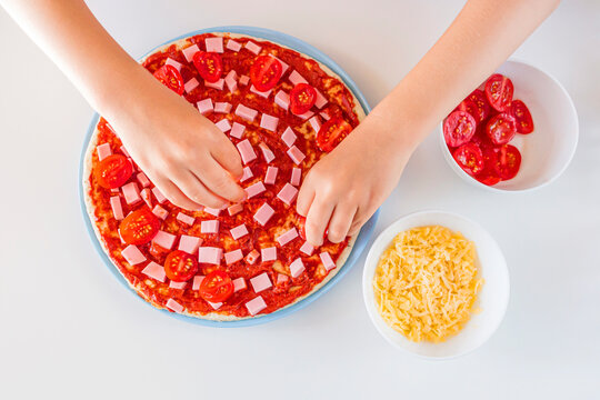 Process of cooking homemade pizza by child. Step 4 kid's hands spreads slices of cherry tomatoes on a dough. Step by step instruction. Children chef concept - Powered by Adobe