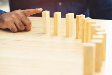 Domino effect. Close up of businessman hand falling wooden block effect from continuous toppled or risk symbolizes a fall, strategy and successful intervention concept.