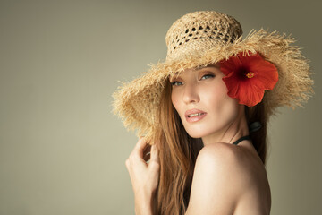 Portrait of a beautiful girl in a straw hat and a red flower in her hair