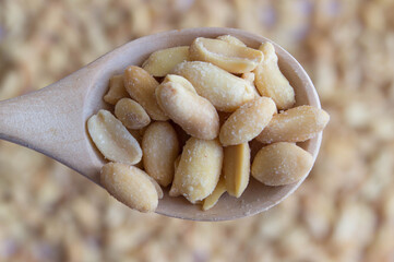 Dry roasted peanuts in wooden spoon isolated on peanut background. Top view.