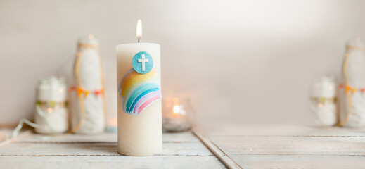 Kommunion, Konfirmation, Firmung, Taufe, Glaube - Weiße Kerze mit Regenbogen und Kreuz auf weißem Holz mit Lichtern und Vasen im Hintergrund