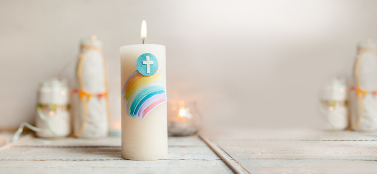 Kommunion, Konfirmation, Firmung, Taufe, Glaube - Weiße Kerze mit Regenbogen und Kreuz auf weißem Holz mit Lichtern und Vasen im Hintergrund
