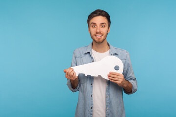 Portrait of positive handsome man in worker denim shirt holding huge paper key and smiling...