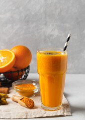 Turmeric smoothie in glass with ingredients, powder, ginger and spice on white or light grey background