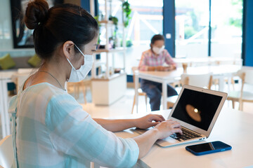 Obraz premium Asian woman wearing face mask and keep social distanicng by sitting on each table in the restaurant during covid-19 or coronavirus outbreak. new normal lifestyle concept