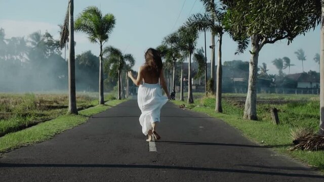 European brunette girl running on the empty road with palm trees in the bali