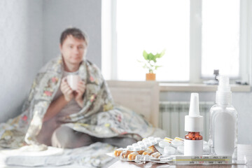 Obraz na płótnie Canvas A sick guy is sitting at home on a sofa with a handkerchief and is taking medicine. Selective focus