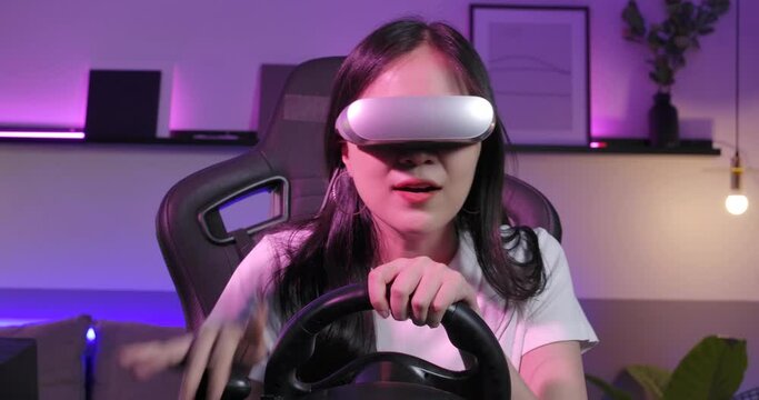 Excited young asian gamer wearing vr glasses sitting in the racing seat simulator cockpit with steering wheel and playing in car racing game, win and cheer with fist gesture. POV monitor screen view.
