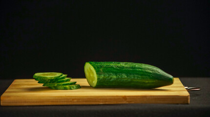 Green cucumber is cut into pieces. Lies on a wooden board on a black background