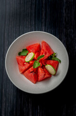 watermelon slices mixed with mint leaves and lemon slices in a white bowl