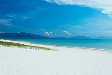 view of sandy sea beach. Calm waves, foam. Blue sky with white clouds. An empty long beach, ocean and mountain background