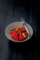 watermelon slices mixed with mint leaves and lemon slices in a white bowl
