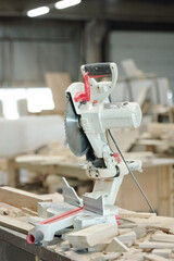 Modern powerful circular saw placed on desk among wooden pieces in carpentry workshop