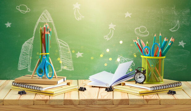 Back to school concept with rocket sketch, pencils and notebook on wooden table over chalkboard background