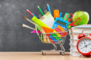 Various office supplies for school in a cart, textbooks, alarm clock and green Apple, on a wooden...