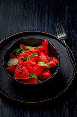 freshly cut  watermelon salad kept in a black bowl and  plate on dark a background