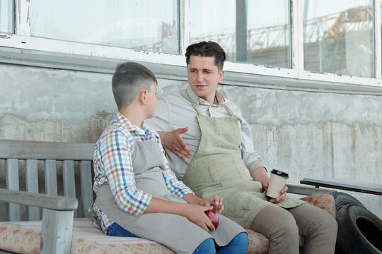 Middle-aged Father Drinking Coffee And Talking To Teenage Son While Resting On Bench Near Garage