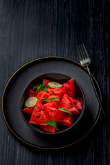 freshly cut  watermelon salad kept in a black bowl and  plate on dark a background