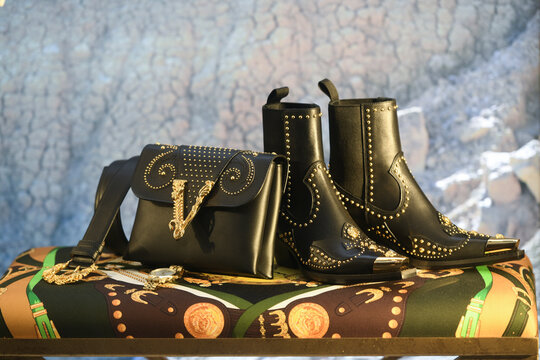 Milan, Italy - January 11, 2020: Black and golden Versace leather boots, belt and purse display
