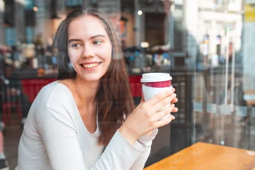 Foto op Plexiglas Jonge vrouw in een café genieten van een kopje koffie - Mooie brunette zit achter een raam in een café-bar in Londen, wegkijkend van de camera, rode bus in de reflectie - Lifestyle en eten drinken concepten © william87