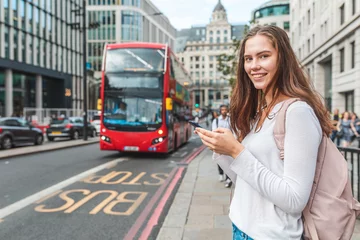 Photo sur Plexiglas Bus rouge de Londres Smiling woman with smartphone at bus stop in London - Portrait of a smiling girl using her phone to check bus timetable on a day out in London - Lifestyle and transportation concepts