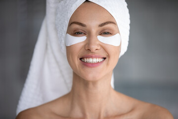 Close up portrait of smiling young woman after shower apply moisturizing under eye patches,...