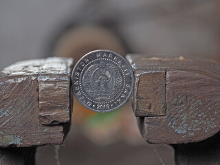 Uzbek coin som clamped in a metal vise. Currency and uzbekistan economy under the onslaught, the concept of financial problems and crisis