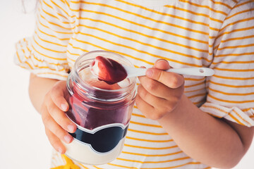 Little girl eat milky dessert with cream and fruity jelly in a jar