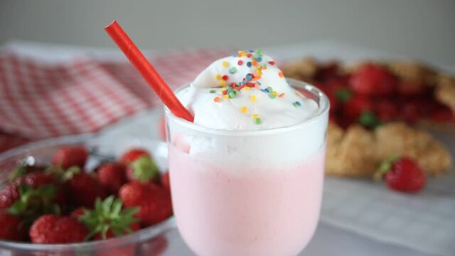 Woman hand put on a table a glass with strawberry smoothie milk shake cocktail with whipped cream