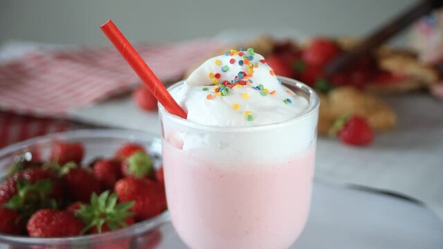 strawberry smoothie milk shake cocktail with whipped cream. On the background woman's hand cut a strawberry tart